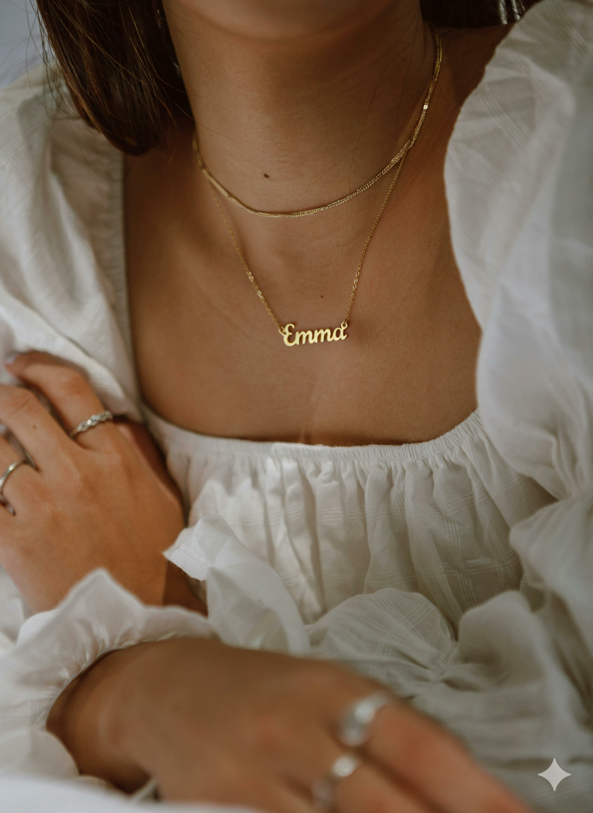 Person wearing a gold necklace with the name 'Emma' on a blurred background